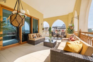 A spacious balcony with wicker furniture, a glass door leading to a terrace, and a view of the cityscape. - Large Terrace and Pool View - 2 Br - Next to Mall (Dubai)
