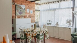A cozy dining area with a wooden ceiling, a dining table with chairs, a white cabinet, and a window with curtains. - Montereale Holiday Home (Realmonte)