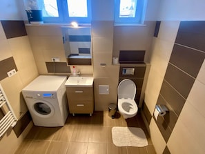 A compact bathroom with a washing machine, sink, toilet, and a small window.