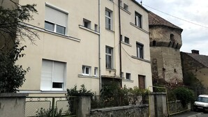 Um edifício residencial de vários andares com fachada bege, várias janelas e uma parede de pedra adjacente ao prédio.