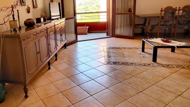 A spacious living room with a large window, a dining area, and a kitchen with a cabinet and a TV. - Belvedere House Noto Alta (Noto)