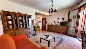 A living room with a sofa, a coffee table, a cabinet with dishes, and a chandelier. - Belvedere House Noto Alta (Noto)