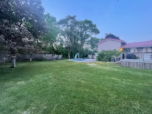 A backyard with a swimming pool, a wooden fence, and a house with a red roof.