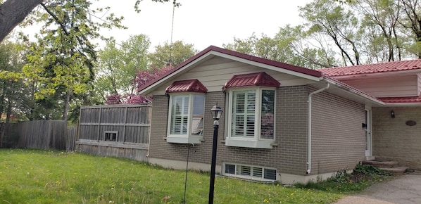 A two-story brick house with a red roof and white trim, a front porch, and a wooden fence.