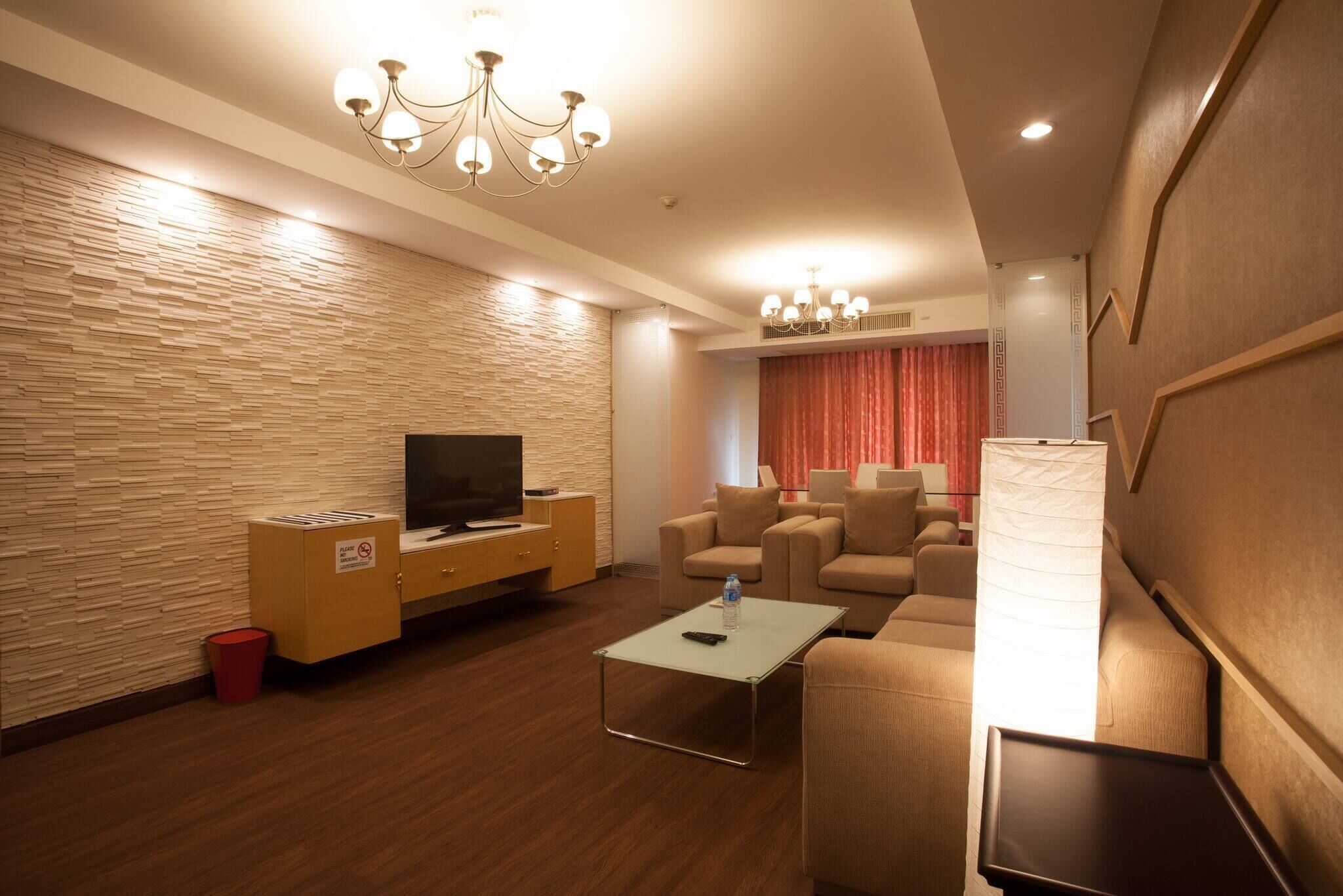 A modern hotel room with a flat-screen TV, a sofa set, a coffee table, and a decorative wall.