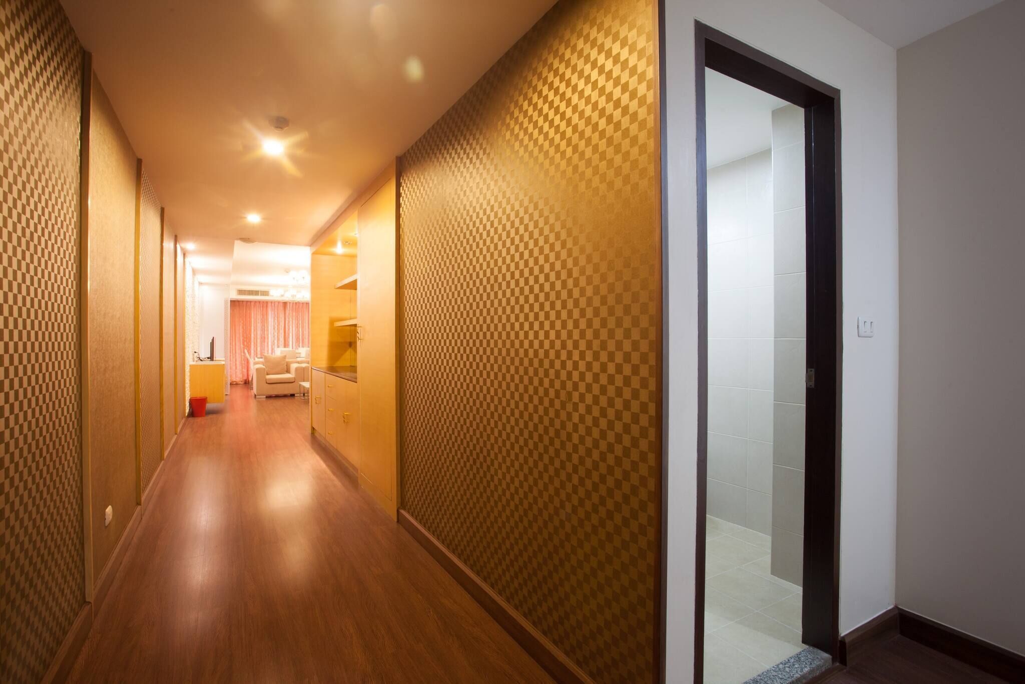 A hotel corridor with wooden flooring, checkered wall panels, and a visible bathroom entrance.