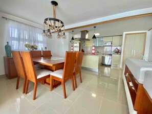 A modern kitchen with a central island, wooden dining table with chairs, and a chandelier.