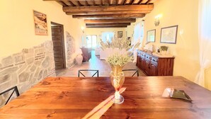 A wooden dining table with a vase of flowers, a stone wall, and a kitchen area with cabinets and a countertop. - Detached Villa - Sleeps 10 - Pool - Pergola - Playground for Children - Wifi (Todi)