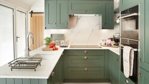 A kitchen with green cabinets, a marble backsplash, and a stainless steel oven.