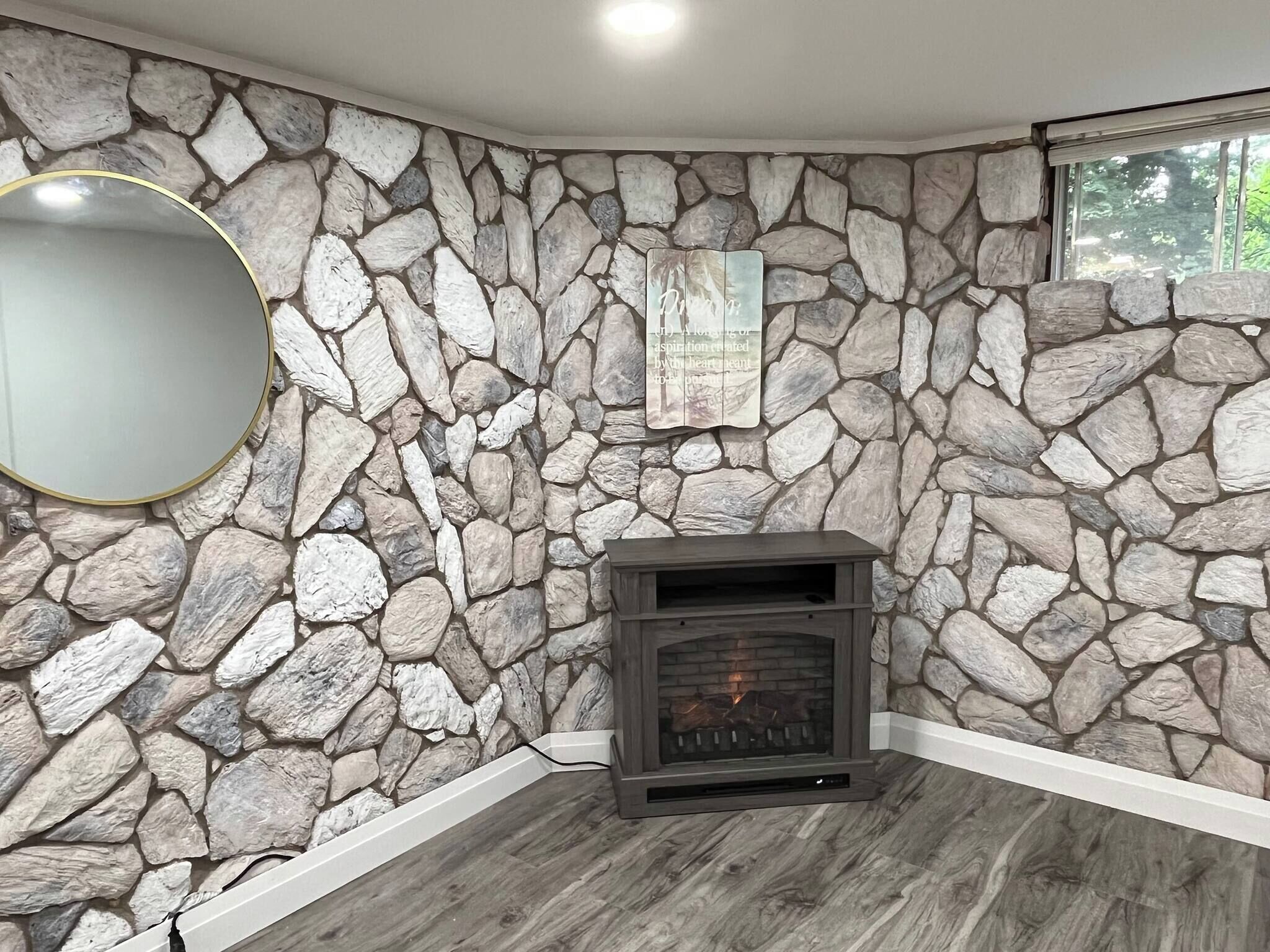 A room with a stone wall, a fireplace, a mirror, and a window.