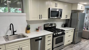 A modern kitchen with white cabinetry, stainless steel appliances, and a marble countertop. - Adorable 1 Bedroom Suite With Kitchen & (Cambridge)