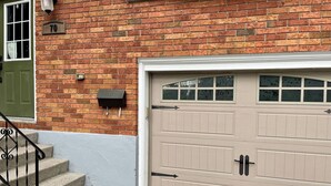 A two-car garage with a beige door, a brick wall, a mailbox, and a green door. - Adorable 1 Bedroom Suite With Kitchen & (Cambridge)