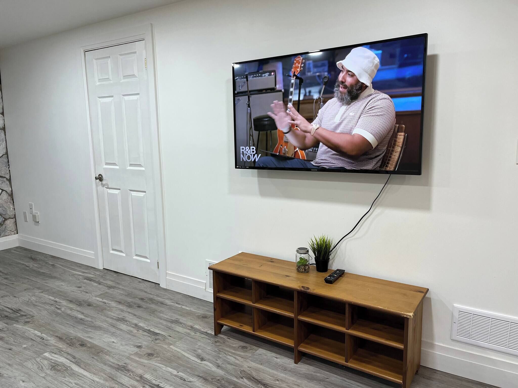Una habitación con una televisión montada en la pared, una mesita de madera y una puerta blanca.