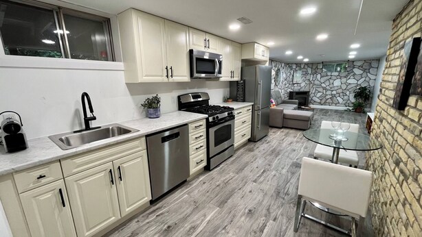 A modern kitchen with stainless steel appliances, a dishwasher, and a dining area with a glass table. - Adorable 1 Bedroom Suite With Kitchen & (Cambridge)