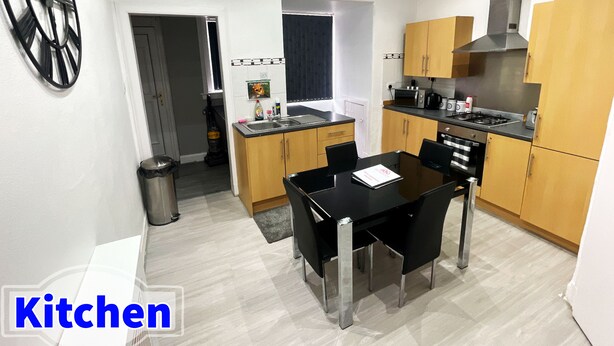 A modern kitchen with wooden cabinets, a black dining table, and a stainless steel sink. - Luxury 3 Bedrooms Entire Flat - Self Check in & Check out (Cowdenbeath)