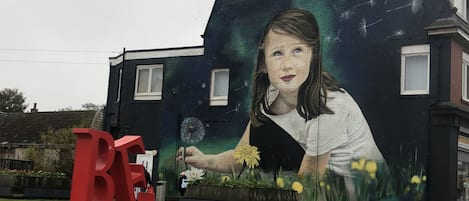 A mural on a building with a large red 'B' sculpture in front.