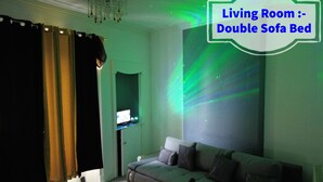 A living room with a double sofa bed, a television on a stand, and a wall with a light projection. - Luxury 3 Bedrooms Entire Flat - Self Check in & Check out (Cowdenbeath)