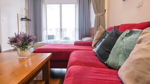 A modern hotel room with a red sofa, a wooden table with a vase of flowers, and a bed with a grey headboard. - Wind Chimes Hideaway - Apartment In Central Hanoi (Hanoi)