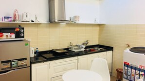 A compact kitchen with white cabinets, a stainless steel range hood, a microwave, and a small dining area with a white table and chair. - Wind Chimes Hideaway - Apartment In Central Hanoi (Hanoi)