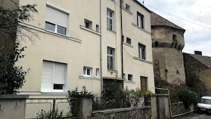 Ein mehrstöckiges Wohngebäude mit beiger Fassade, zahlreichen Fenstern und einer angrenzenden Steinmauer.