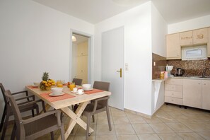 A dining area with a table set for two, a kitchen with a microwave and a coffee maker, and a door leading to another room. - Icabaru Private House With Garden & Bbq, Near Laganas, Zakynthos (Zakynthos)