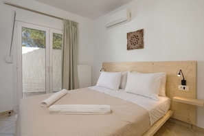 Une chambre à coucher comprenant un lit, une table de chevet, un climatiseur fixé au mur et une fenêtre avec des rideaux.