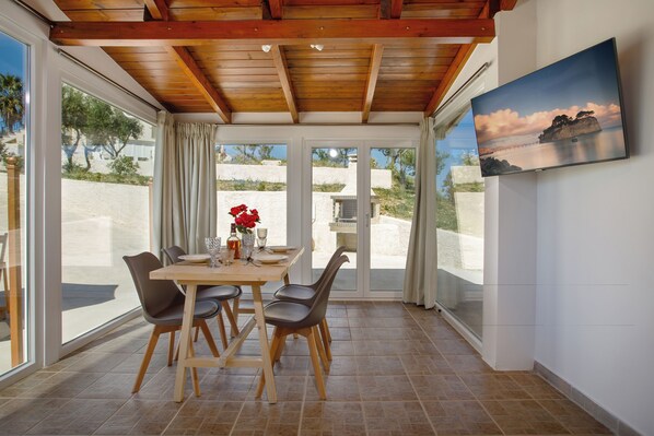 A dining area with a table and chairs, a painting on the wall, and large windows with a view of the outdoors.