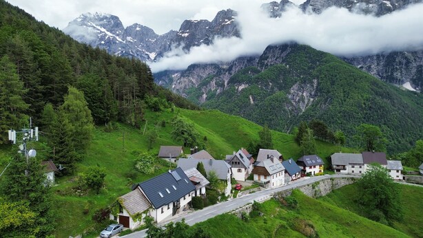A village with traditional houses, a winding road, and mountains in the background. - Apartma Pohar- A Bit Different! (Bovec)