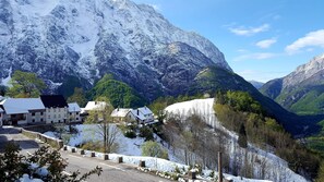A mountainous landscape with snow-covered peaks and a valley with buildings. - Apartma Pohar- A Bit Different! (Bovec)