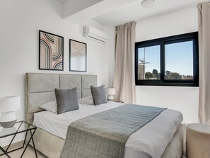 A modern bedroom with a large bed, two pillows, a bedside table with a lamp, and a window with curtains. - Sanders River Plaza Nice 3 Bedroom Apt w Terrace (Limassol)