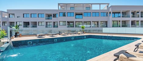 A modern hotel with a large pool, sun loungers, and a clear view of the building's architecture.