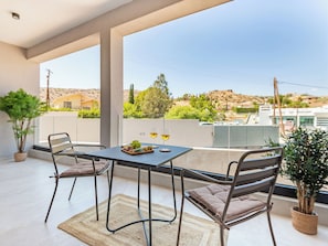 Varanda com mesa posta para dois, com uma garrafa de vinho e um prato de uvas.