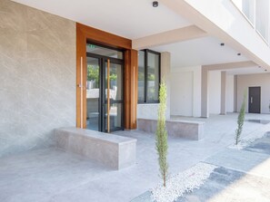 Une entrée moderne avec une porte en verre, un cadre en bois et un petit arbre au premier plan.
