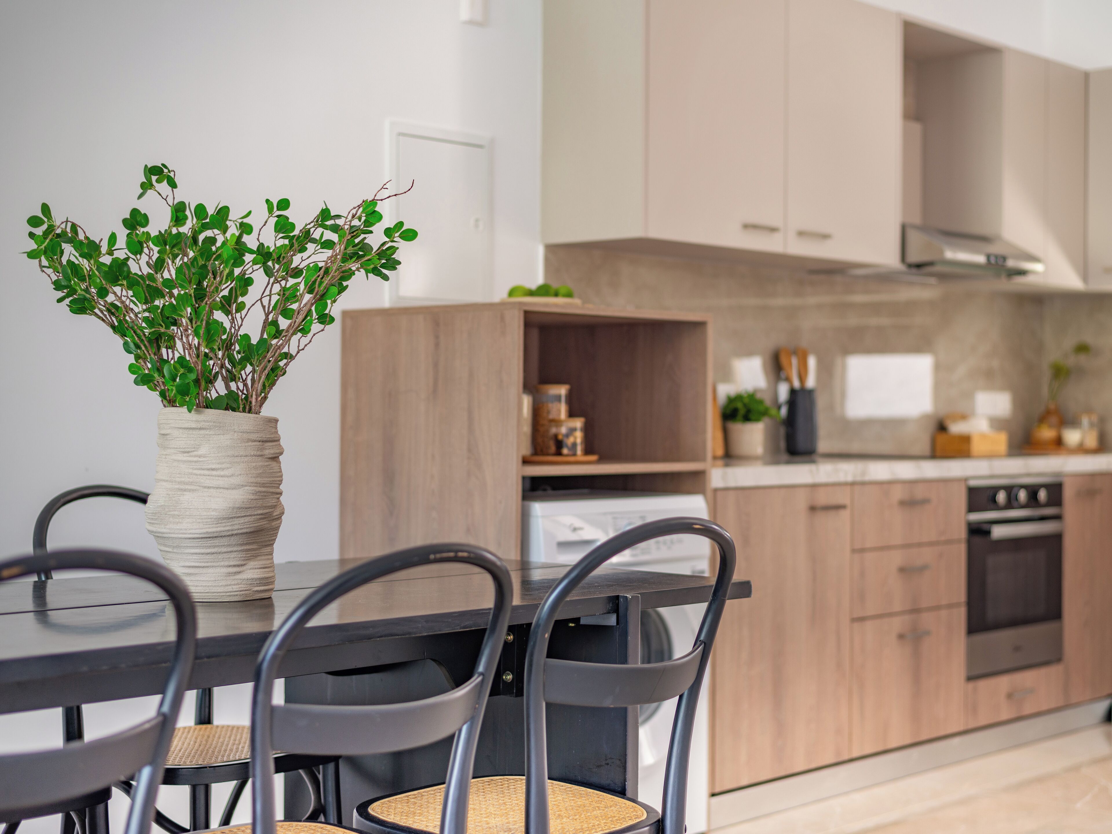 A modern kitchen with wooden cabinets, a dining table with chairs, and a potted plant on the table.