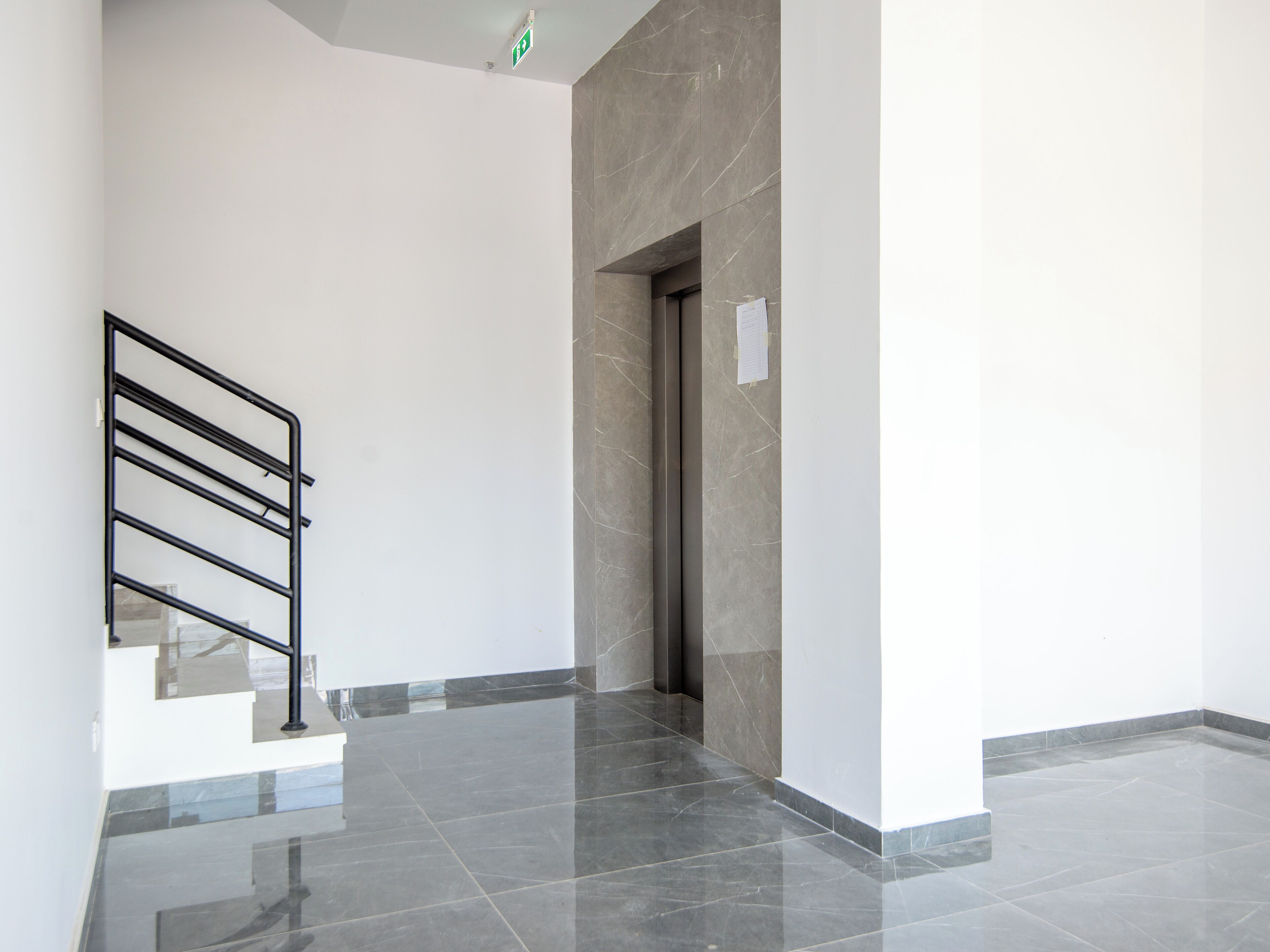 Un couloir propre et moderne, avec un escalier en métal, un mur en marbre et une porte.