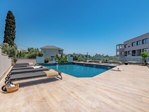 Ein Pool auf dem Dach mit Liegestühlen, einem strahlend blauen Himmel und modernen Gebäuden im Hintergrund.