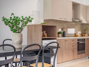 A modern kitchen with wooden cabinets, a dining table with chairs, and a potted plant on the table. - Sanders River Plaza - Jolly 2 Bedroom Apartment With Balcony (Limassol)