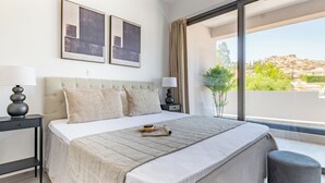 A modern bedroom with a large bed, two bedside tables, a window with a view of a mountainous landscape, and two framed pictures on the wall. - Sanders River Plaza - Jolly 2 Bedroom Apartment With Balcony (Limassol)