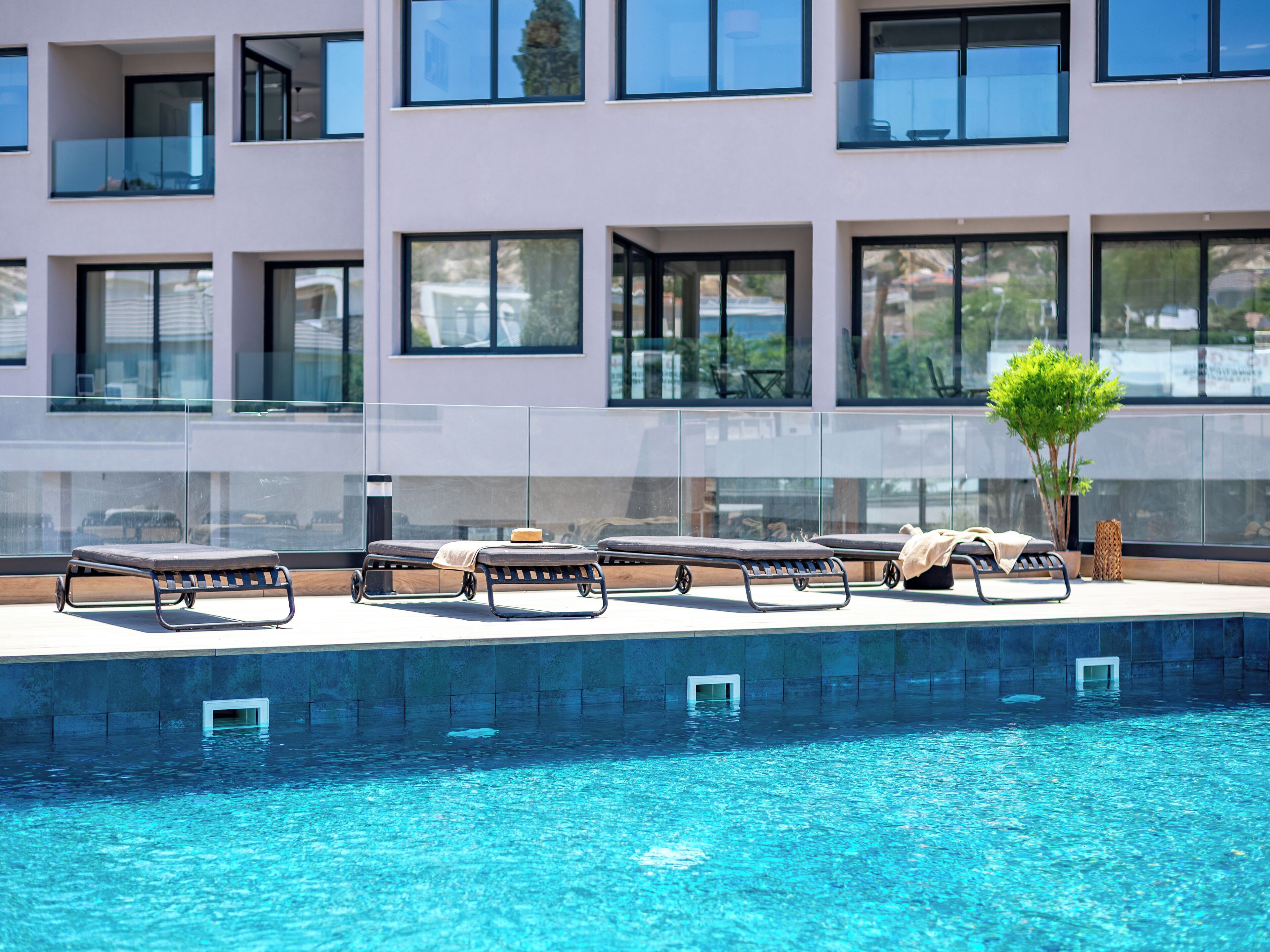Uma área de piscina moderna com espreguiçadeiras e guarda-corpo de vidro.