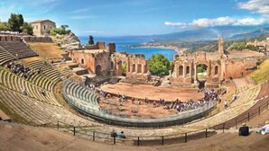 An ancient amphitheater with tiered seating and ruins in the background.