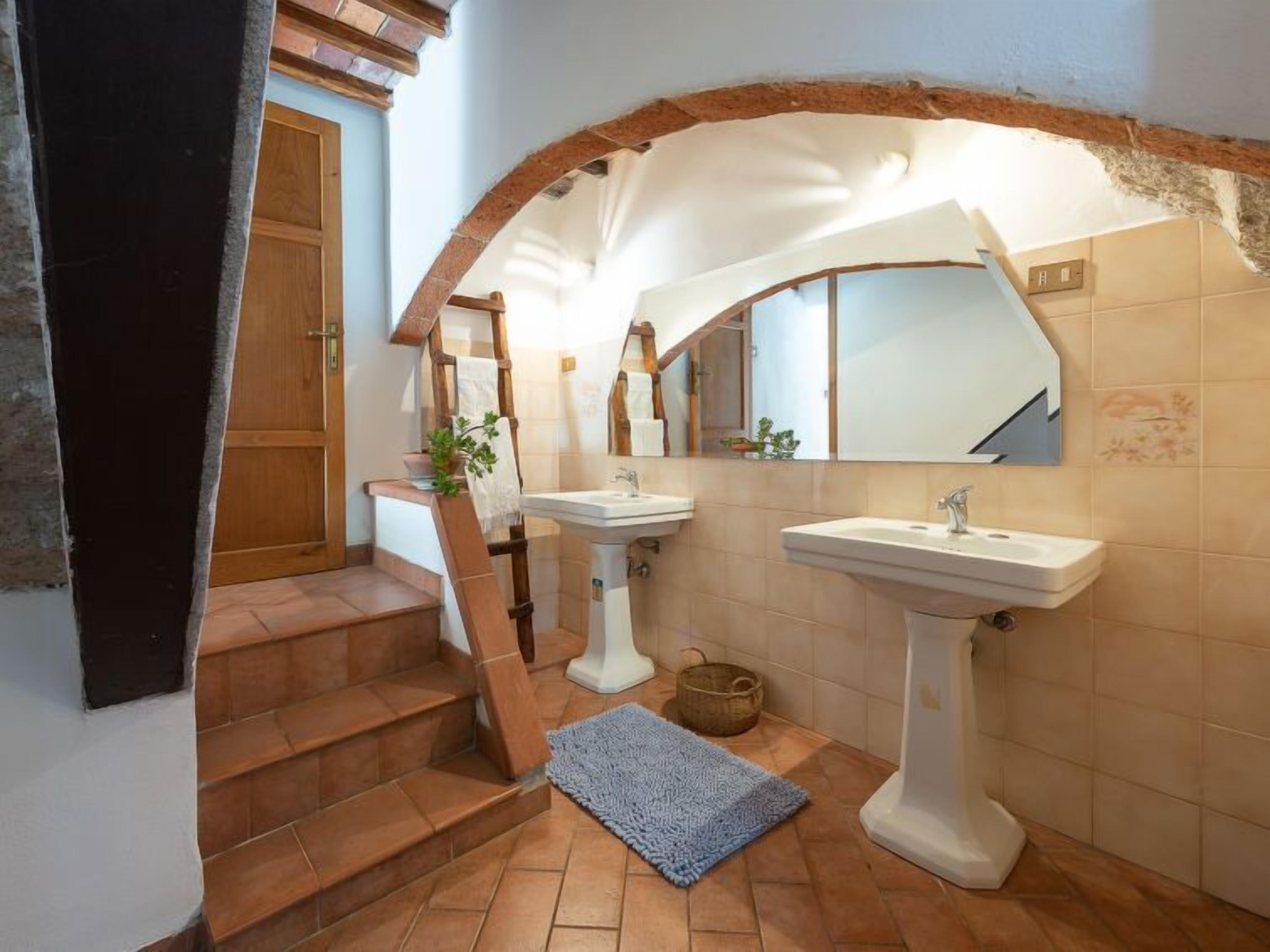 A bathroom with two sinks, a mirror, and a staircase leading to a wooden door.