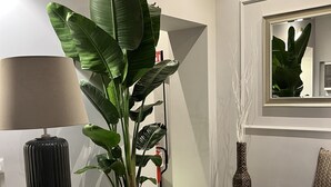 Una sala de estar moderna con una planta grande en maceta, una lámpara, un sofá negro, un espejo y un equipo de aire acondicionado.