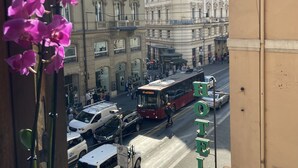 Vista de la calle con un edificio que dice "HOTEL" y un autobús rojo al fondo.
