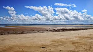 Une plage avec une vaste étendue de sable et un ciel dégagé parsemé de quelques nuages.