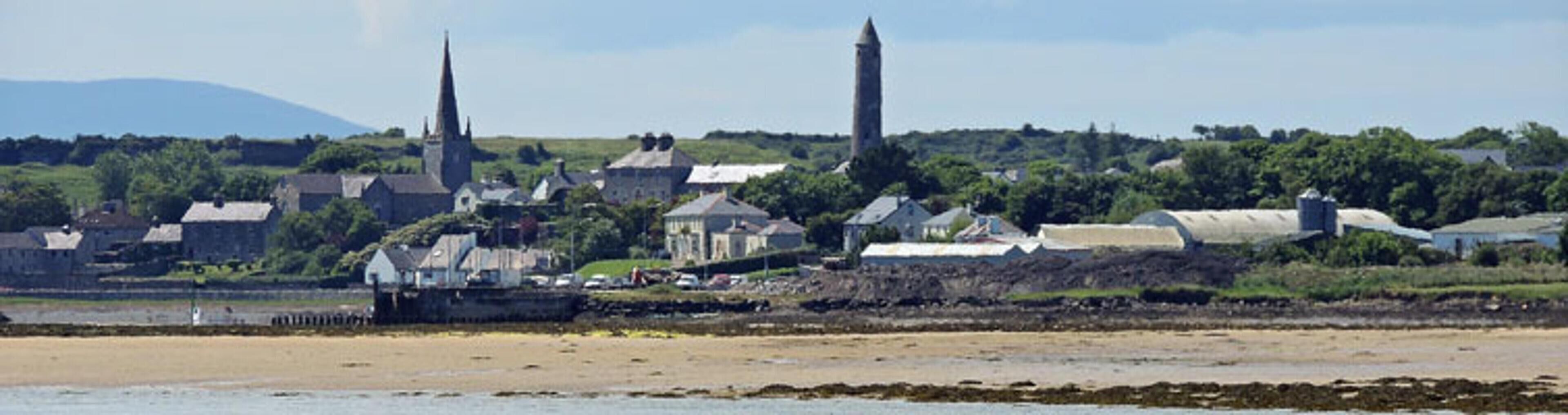 Uma cidade costeira com edifícios históricos, incluindo uma igreja com uma torre alta, e uma praia arenosa em primeiro plano.