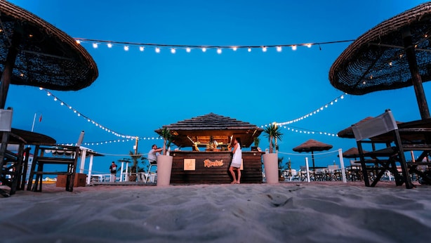 A beach bar with a thatched roof, string lights, and palm trees. - AmaRèmin - LIVING RIMINI - Modern apartment overlooking the sea (Rimini)
