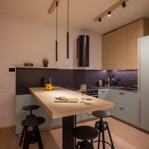 Una cucina moderna con isola centrale, sgabelli da bar, un bicchiere di vino e una ciotola di frutta.