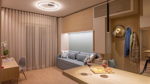 A modern, well-lit room with a sofa, a dining table with a wine glass and cheese board, and a desk with a plant. - AmaRèmin - LIVING RIMINI - Modern apartment overlooking the sea (Rimini)