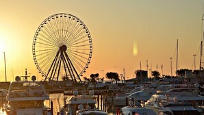 A marina with multiple boats docked, a prominent Ferris wheel in the background, and the sun setting or rising. - AmaRèmin - LIVING RIMINI - Modern apartment overlooking the sea (Rimini)