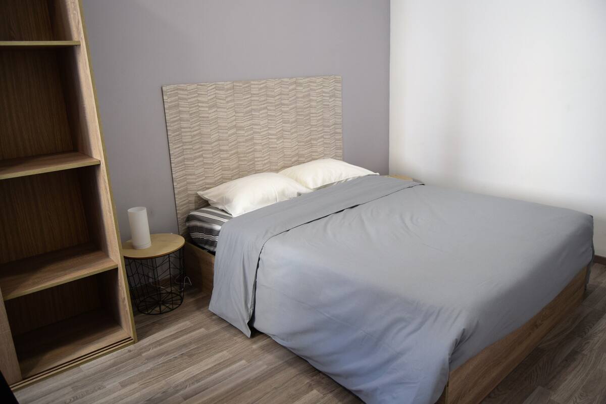 A bedroom with a bed, a wooden nightstand, a round side table, and a built-in shelving unit.